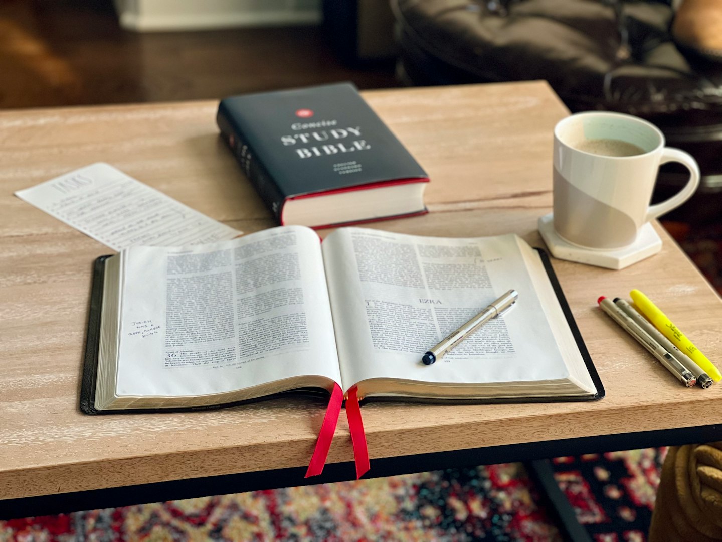 Open Bible and study supplies arranged on a wooden table.